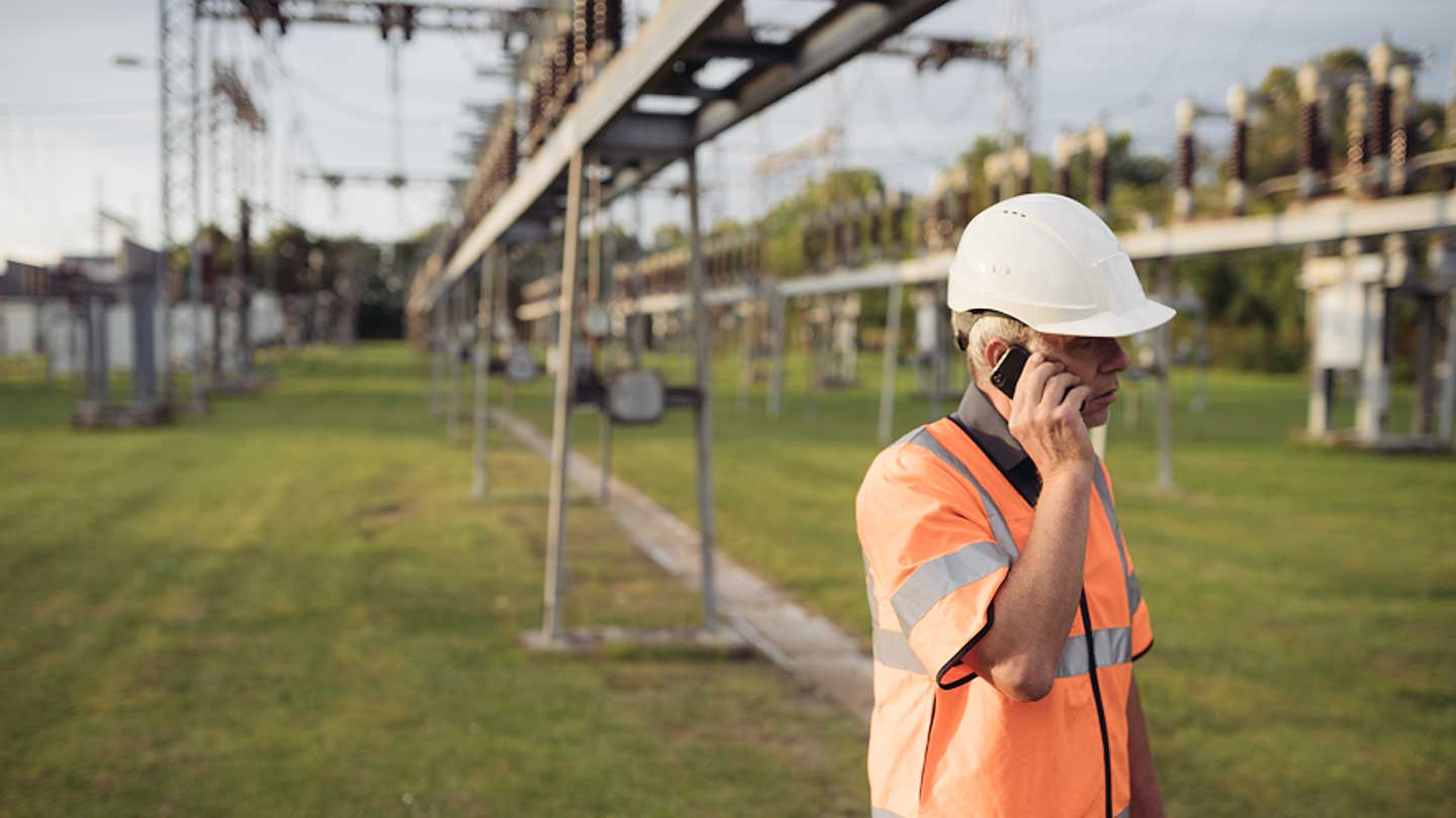 A man wearing a high visibility jacket and hard hat speaks on a mobile phone.