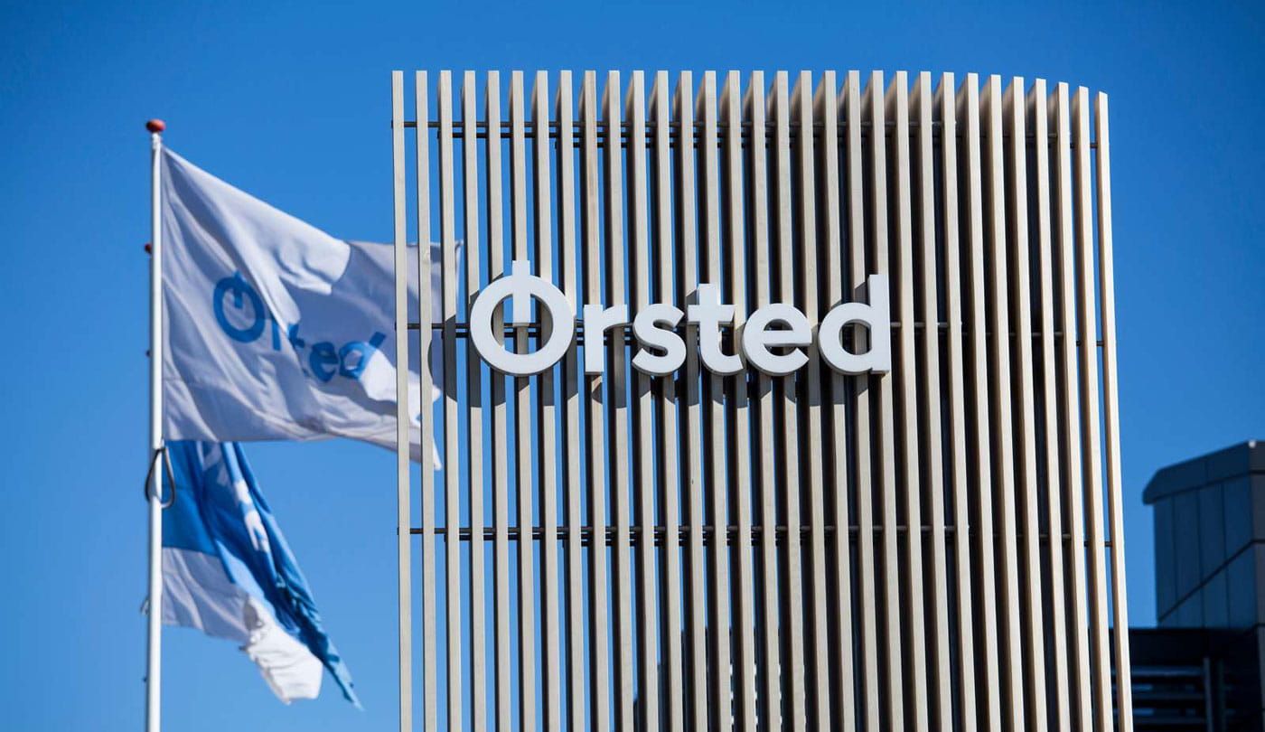 Cartaz da Ørsted e duas bandeiras do lado de fora de um dos escritórios da Ørsted em um dia ensolarado.