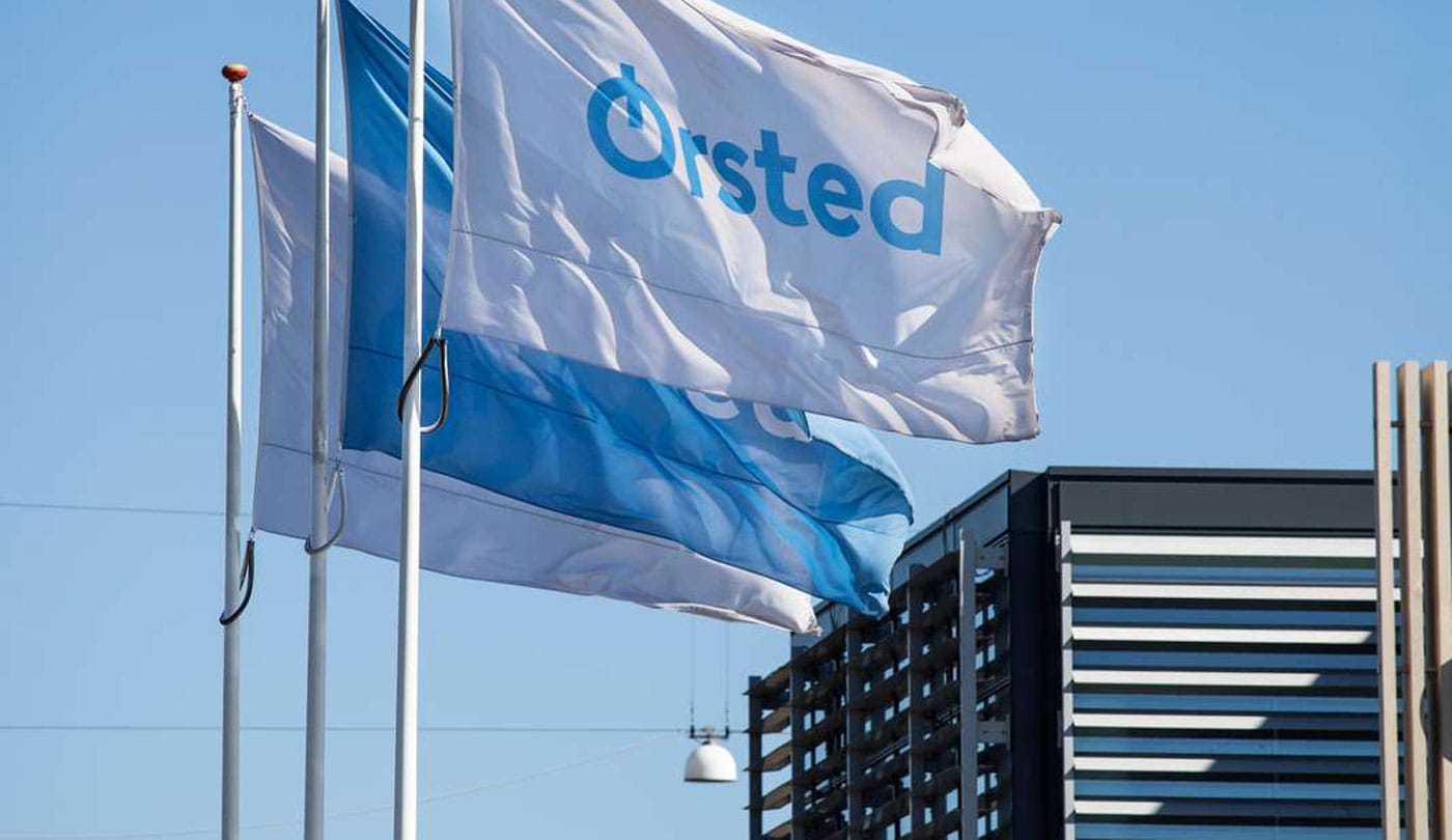 3 Ørsted flags fly outside of an Ørsted office on a sunny day.