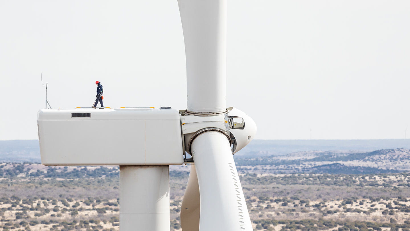 A person wearing safety gear walking on top of an onshore wind turbine.