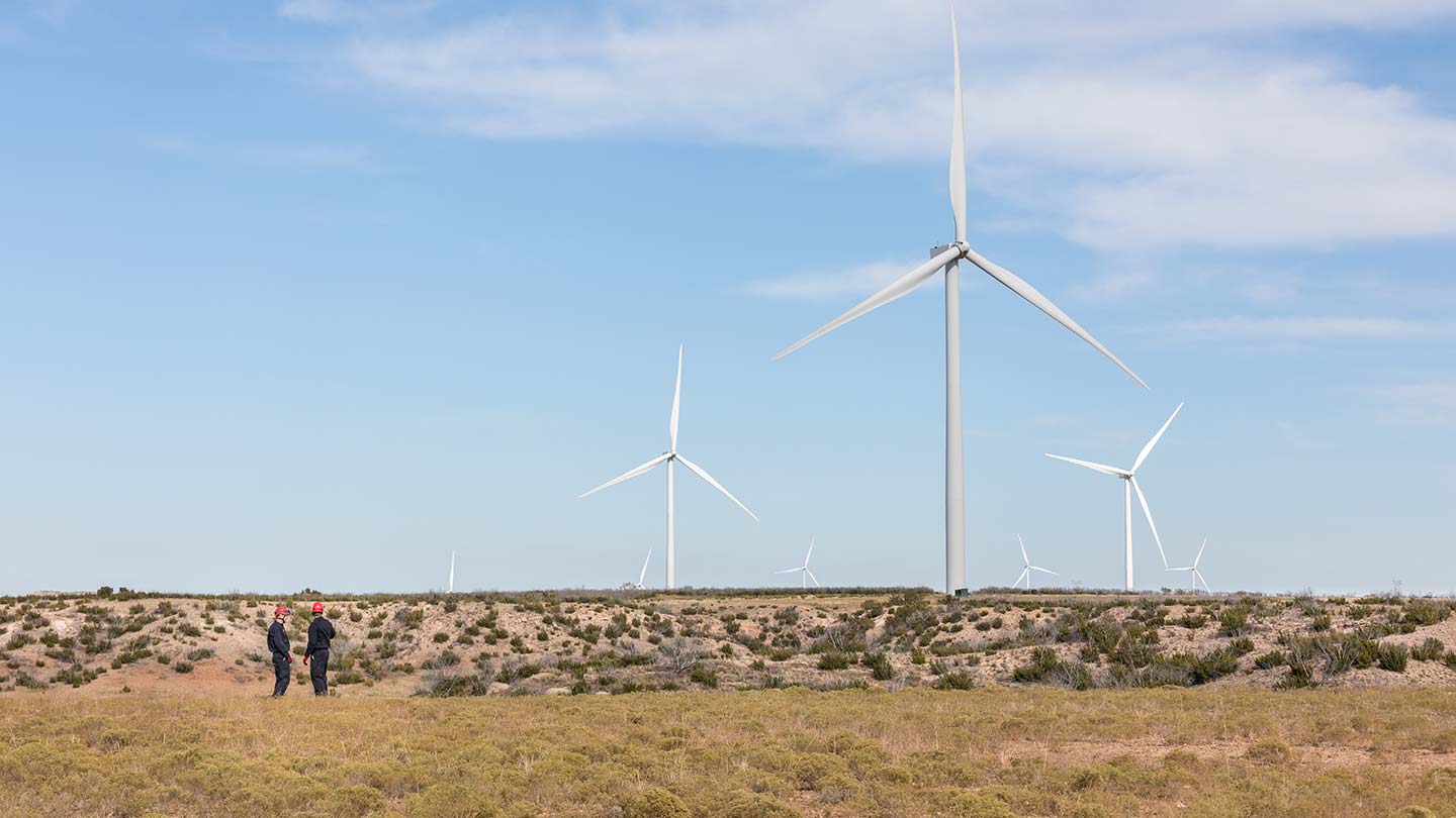 Tres aerogeneradores terrestres Ørsted en una llanura con dos trabajadores observando.