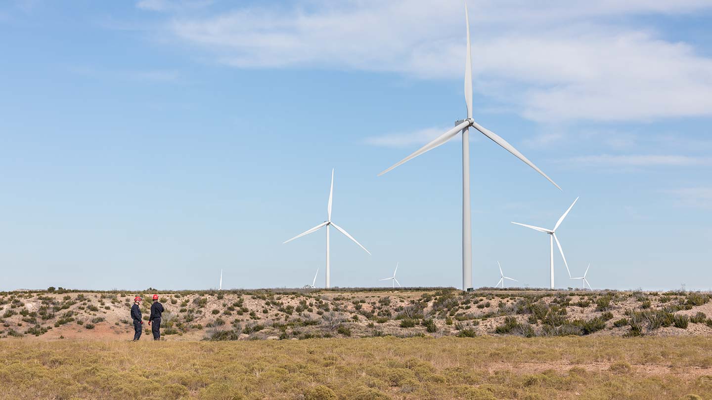 Tre Ørsted vindturbiner på land står på en slette med to arbeidere som ser på.