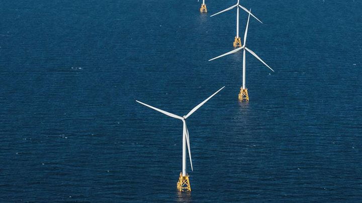 Four offshore wind turbines stand on a dark blue sea, part of Ørsted's growing offshore wind portfolio in the U.S.