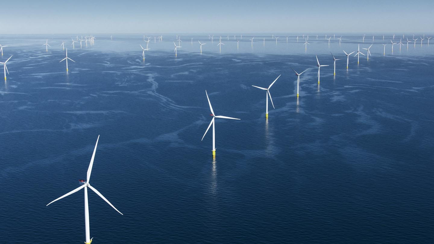 The world's largest offshore wind farm, with several Ørsted wind turbines standing in rows in dark blue ocean.