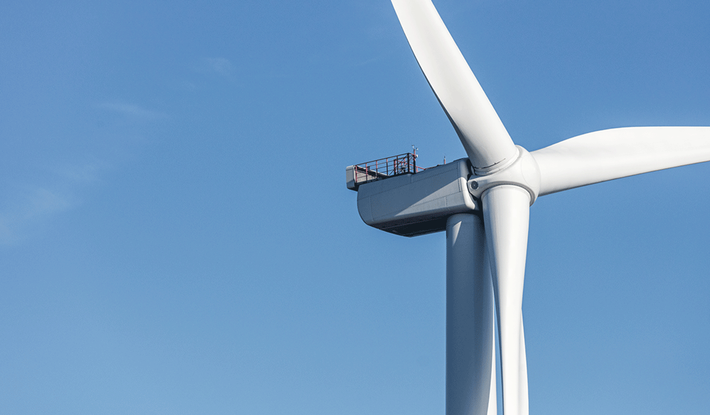 Top of a white Ørsted wind turbine and a clear blue sky.