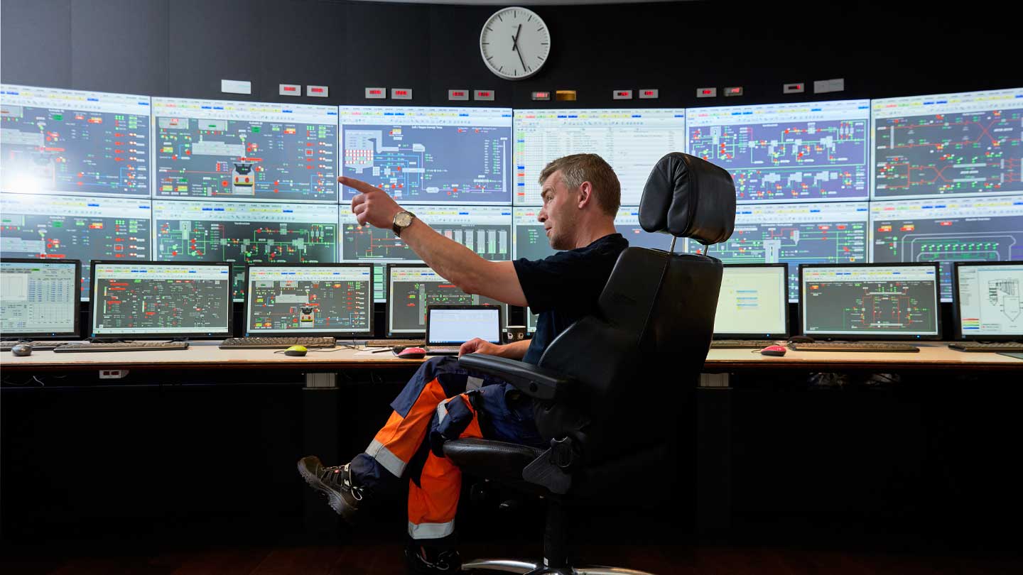 Worker in safety gear sitting in front of a control room monitor.