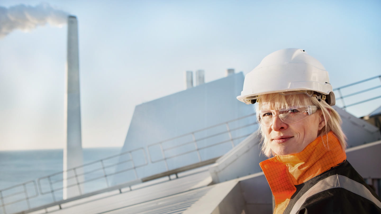 A worker standing on top of a power plant wearing safety gear.