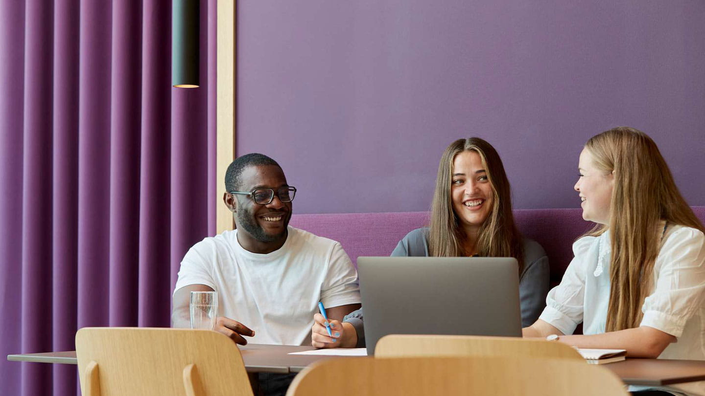 Three Ørsted employees smiling while conducting a meeting in a room with purple walls, a sofa and curtains.
