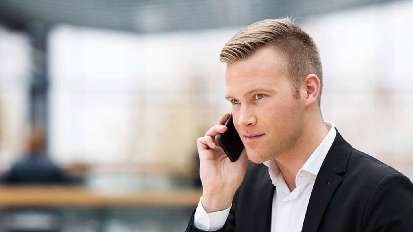 A man in a suit holds a mobile phone up to his right ear.