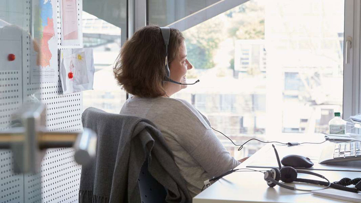 En medarbejder, der sidder ved sin arbejdsplads med en grå bluse på og høretelefoner. 