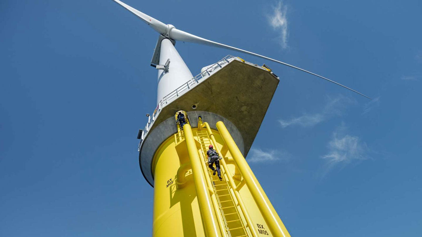Maintenance workers climbing up yellow ladders to reach the top of a wind turbine.