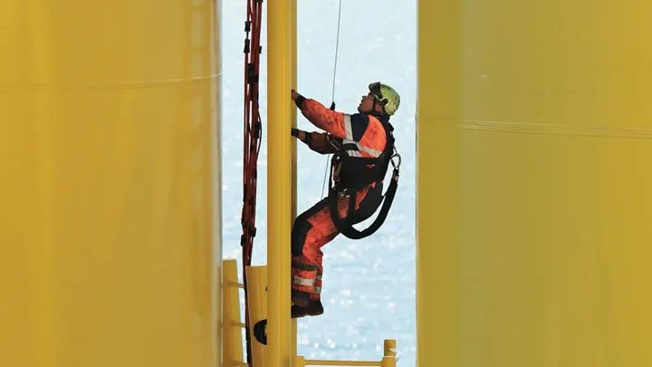 Empregado da Ørsted com equipamento de segurança, subindo a escada de um monopilar de una das turbinas eólicas da Ørsted.