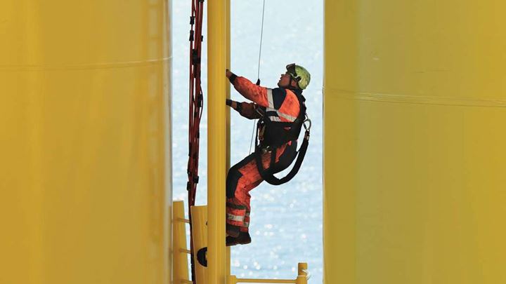 Un impiegato di Ørsted che indossa un elmetto e l'equipaggiamento di sicurezza, salendo su per la scala di un monopalo di una delle turbine eoliche di Ørsted.