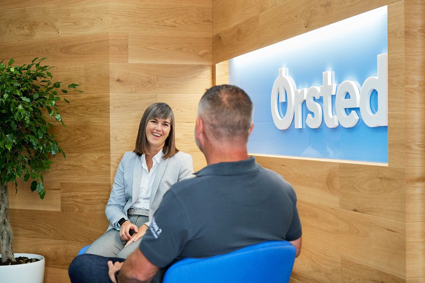 Two employees sitting in front of an Ørsted logo hanging on the wall.