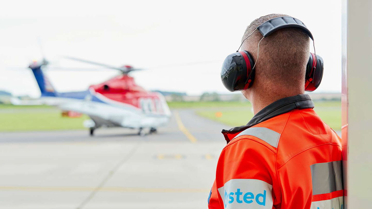 An Ørsted employee wearing protective gear watches on at a helicopter in the distance.