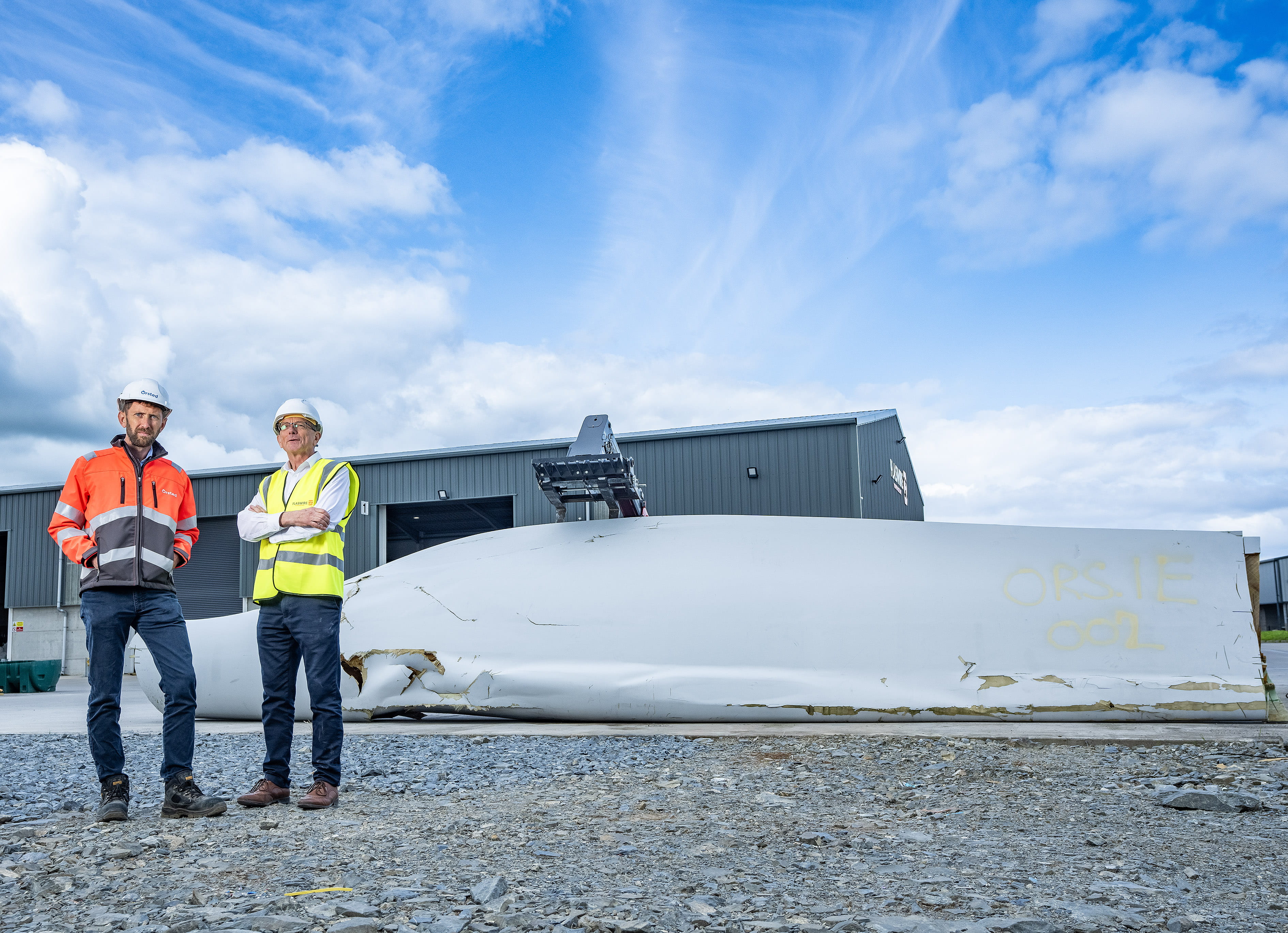 To men standing in front of a turbine blade ready to be recycled