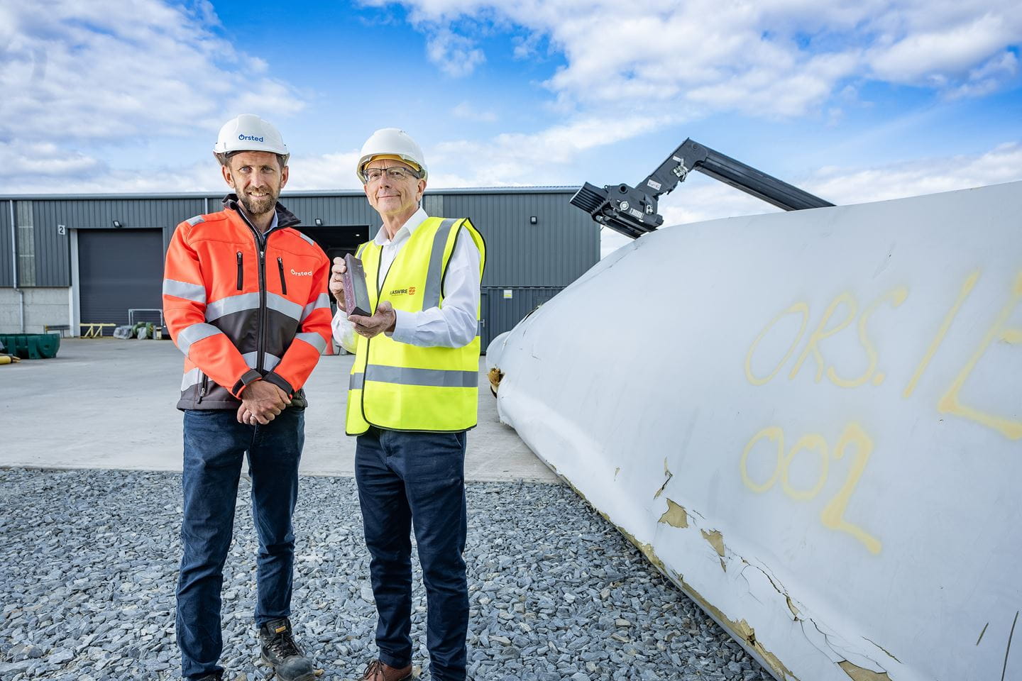 To men standing in front of a turbine blade ready to be recycled