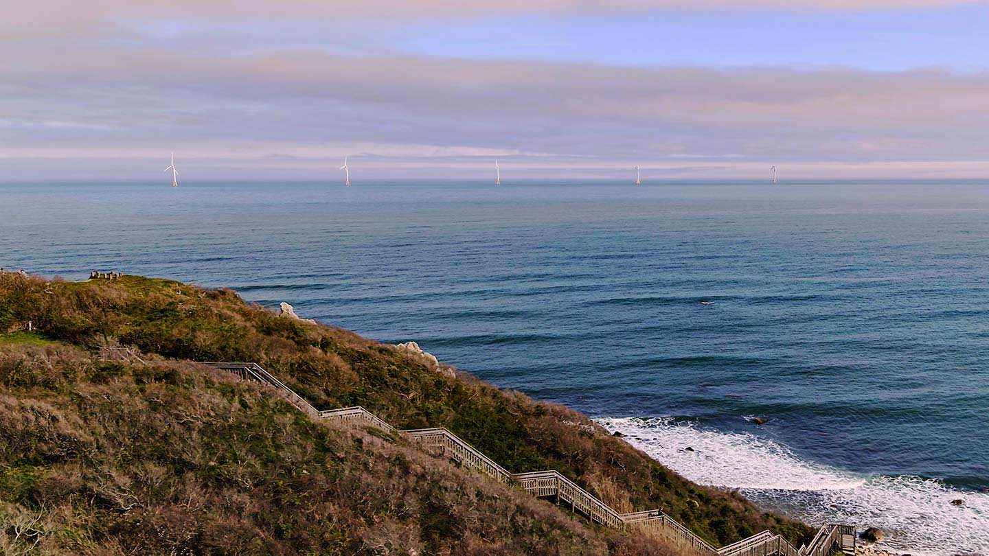 View from the top of a staircase leading down to the beach, with Ørsted's Block Island Wind Farm turbines in the distance.