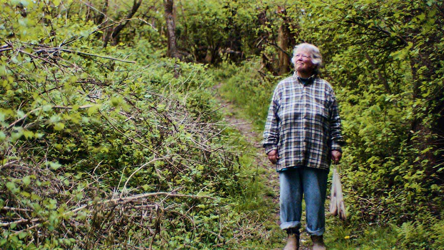 Kim Gaffett, bird bander, Block Island local, and offshore wind supporter, stands on a forest path surrounded by greenery.
