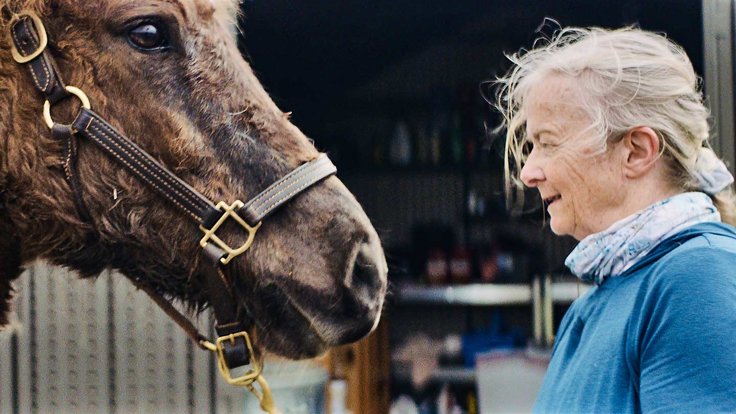 Dr. Susan Gibbons, Block Island local and science teacher, face to face with her horse beside a stable.
