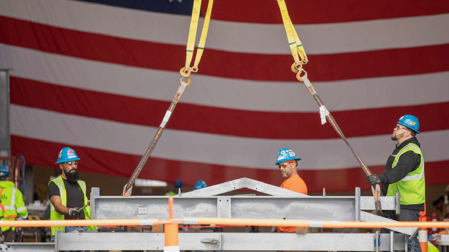 Well-paid union workers hoist equipment in front of an American flag as part of Ørsted’s National Offshore Wind Agreement 