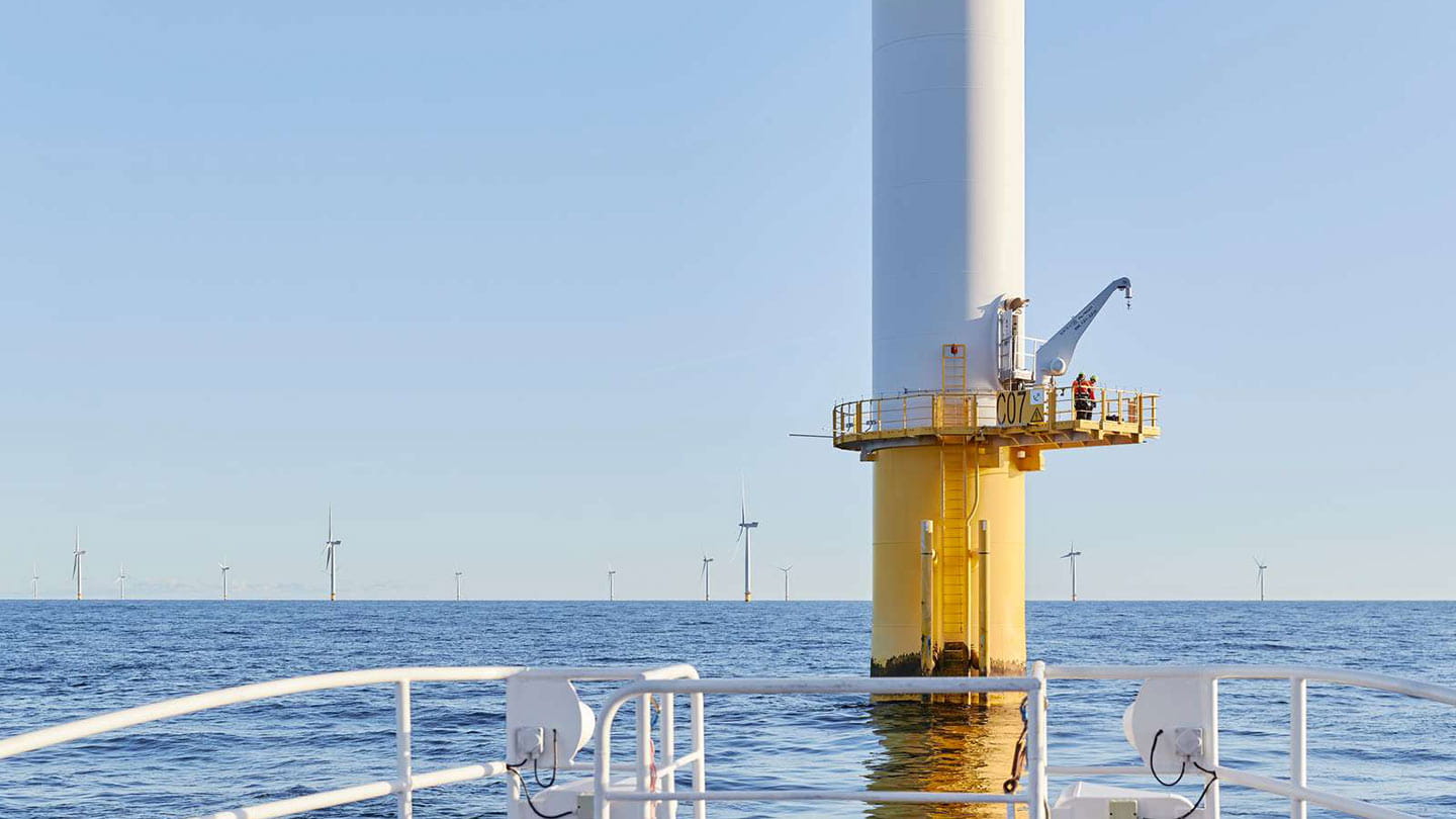 Two workers with a crane on the foundation of an Ørsted offshore wind turbine, working on offshore wind construction.