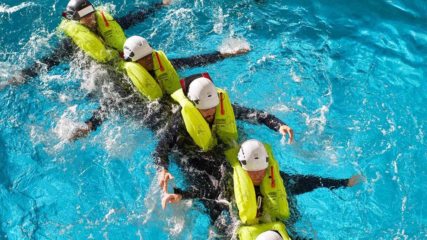 Ørsted workers wearing life jackets undergo safety at sea training in a pool to prepare for offshore wind jobs 