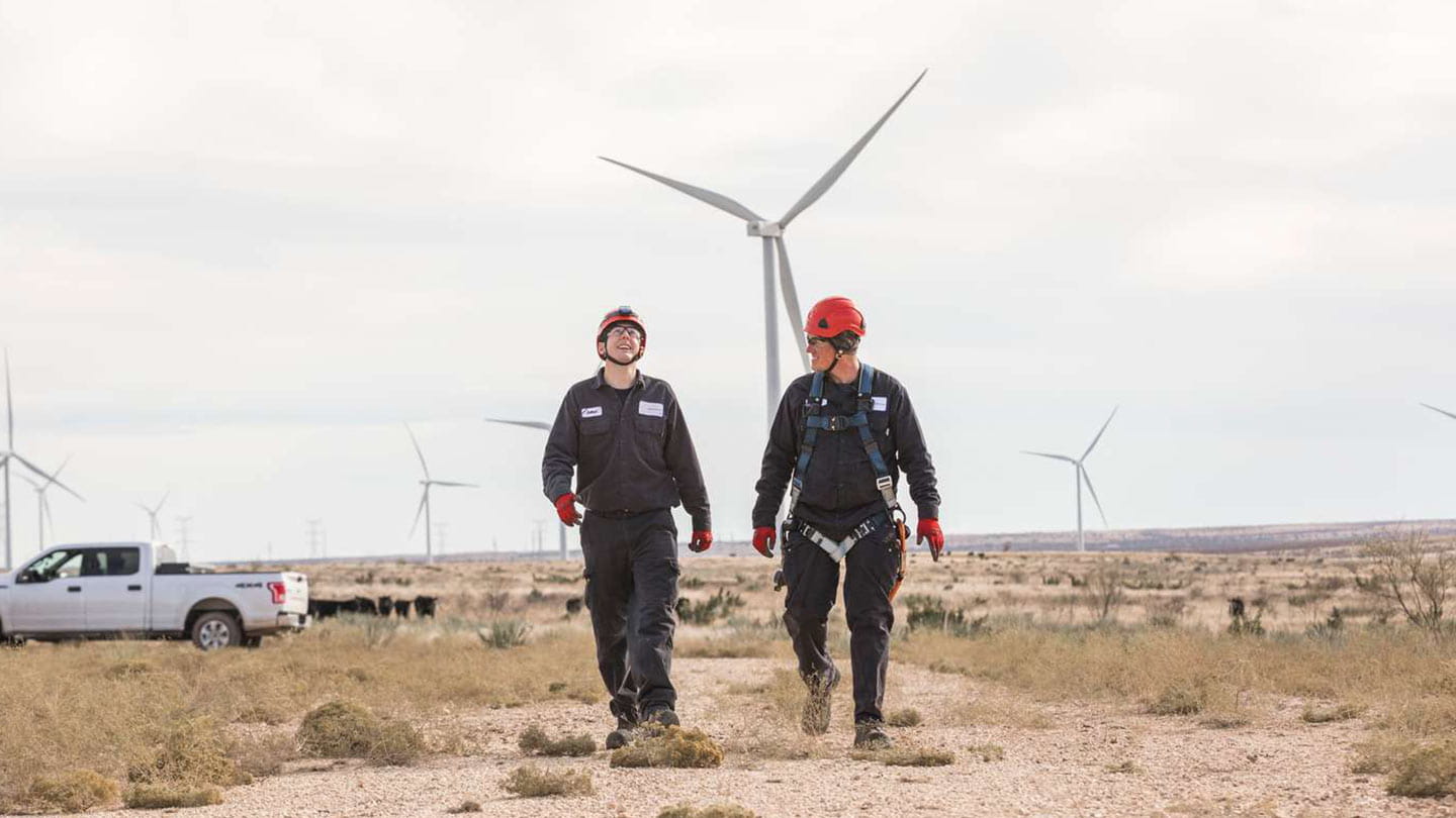 Two Ørsted employees walking in front of onshore wind turbines, working for a sustainable energy company.