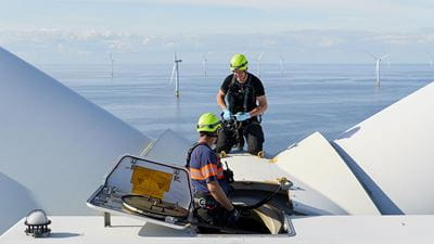 Two &#216;rsted wind technicians on top of an offshore wind turbine, building the clean energy needed for a net-zero economy
