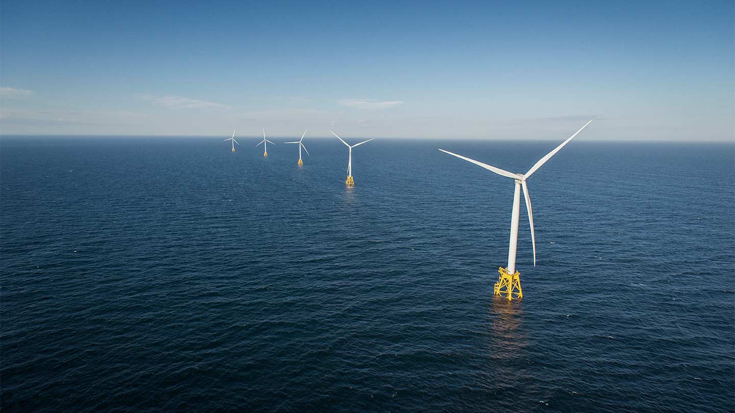 Five offshore wind turbines standing in one line in the middle of the ocean.