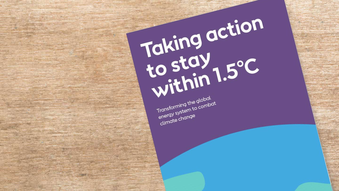A booklet named 'Taking action to stay within 1.5°C' is sat on top of a wooden surface.