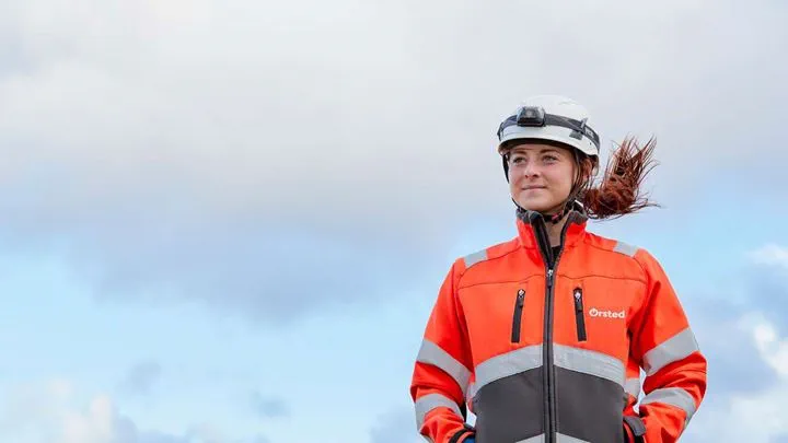 Empregado da Ørsted com capacete e casaco de segurança laranja brilhante olhando à distância.